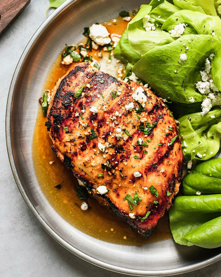roasted garlic herb butter chicken breast on a silver plate with greens on the side
