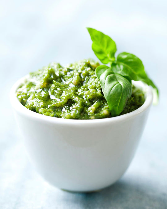 a white deep narrow small bowl filled with pesto and garnished with basil leaves