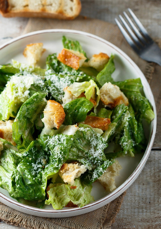 a white bowl with caesar salad tossed with homemade croutons and parmesan cheese