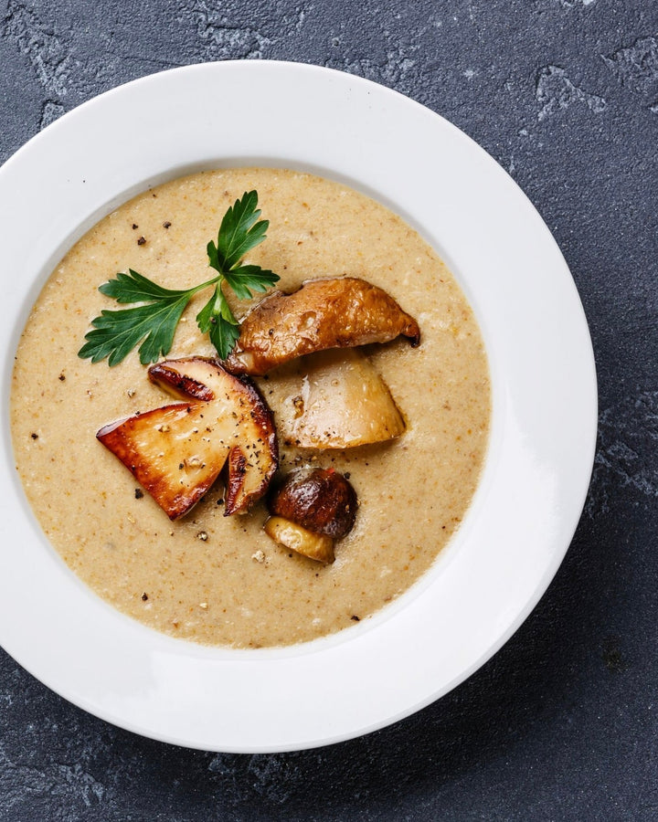 white bowl cream of mushroom soup with mushroom slices floating on top sprig of thyme