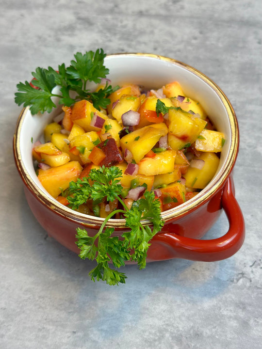 peach salsa, chopped up peaches, jalapeno, red onion, shallots, cilantro, peppers, general yello color in a cute red bowl with two handles and a gold trim with parsley as garnish